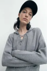 Sweater gris melange de tejido de punto, con capucha y cordones cruzados en el escote.