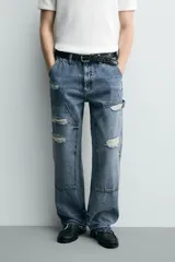 Pantalón de jean estilo carpintero con corte relaxed fit, tiro medio y pierna recta. Presenta un lavado azul medio con efecto desgastado y roturas en las rodillas. Incluye bolsillos laterales tipo plastrón, tira multifunción en la pierna, cierre frontal con cremallera y botón.