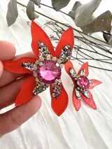 Aros colgantes con forma de flor naranja y centro con gemas rosas y rojas.
