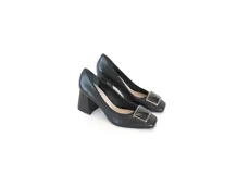 Zapatos de tacón de cuero negro, con punta cuadrada, aplique metálico en el empeine y tacón ancho de altura media con textura geométrica.