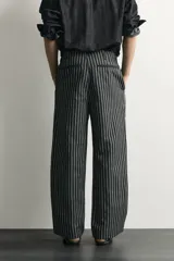 Pantalón relaxed fit de mezclilla con mezcla de algodón y lino, con diseño de rayas verticales oscuras y claras. Cuenta con cintura ajustable con cordón, bolsillos frontales, bolsillo cerillero y cierre frontal con cremallera y gancho metálico.