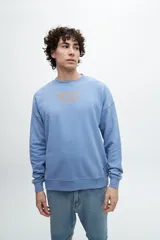 Buzo celeste de corte holgado con cuello redondo y puños y cintura acanalados. Estampado frontal con texto "Sunset Whispers" en color azul.