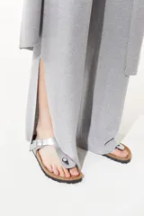 Pantalón gris de tejido de punto confeccionado en lurex. De tiro alto con elástico en la cintura, la pierna se ensancha en el ruedo y cuenta con tajos en los laterales.