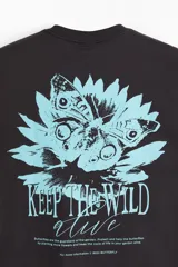 Remera de algodón negra de corte holgado, con cuello redondo y diseño gráfico de una flor celeste y la inscripción "Keep the wild alive" en el pecho.