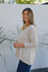 Sweater de tejido de punto en color beige, con cuello redondo, mangas tres cuartos y corte holgado con ruedo ligeramente más largo en la parte posterior.