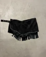 Short pollera negro de efecto gamuza o cuero sintético, con borde festoneado y tachas metálicas plateadas. Presenta flecos largos en el ruedo inferior y se ajusta con una hebilla en el lateral.