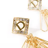 Aros colgantes dorados con forma cuadrada, con letra 'D' calada y strass incrustados.