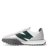 Championes urbanos New Balance, con capellada de gamuza color crema y detalles en blanco y verde. Presenta el logo "N" en cuero verde en los laterales y suela de goma texturizada en gris.