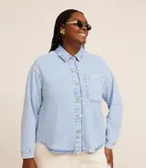 Camisa de jean de algodón, color celeste claro lavado, con cuello tradicional, manga larga y bolsillo de parche en el pecho. Presenta un cierre frontal con botones metálicos.