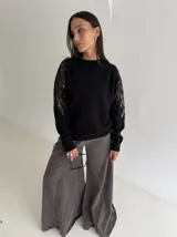 Sweater negro de tejido de punto con cuello redondo y mangas largas. Presenta detalles de transparencias y apliques bordados con pedrería en la parte superior de las mangas.