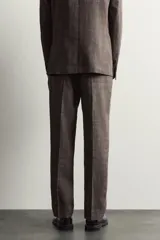 Pantalón de traje regular fit marrón con sutil estampado a cuadros, confeccionado en mezcla de lino y lana. Cuenta con bolsillos delanteros, bolsillos traseros de doble vivo con botón y raya marcada en el centro de las piernas.