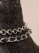 Botas cortas de cuero marrón con textura envejecida, suela track negra con plataforma y taco bajo. Presentan un detalle de tres cadenas metálicas plateadas removibles alrededor del tobillo y cierre lateral interno.