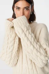 Sweater de tejido de punto grueso en color crudo, con diseño de trenzas en las mangas y cuerpo. Presenta cuello redondo y un calce holgado y confortable.