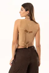 Chaleco de gamuza color beige con estilo western, presenta cierre frontal con botones y detalles de ojalillos metálicos con cordones de cuero entrelazados en la parte superior del frente.