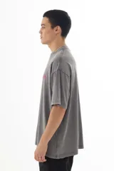 Remera gris con efecto acid wash, corte holgado y estampa pequeña en el pecho con diseño abstracto en color fucsia.