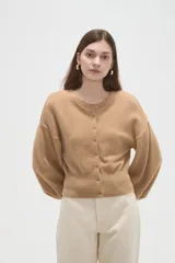 Saco de punto color beige, con cuello redondo, cierre frontal con botones y mangas largas con puños acanalados.