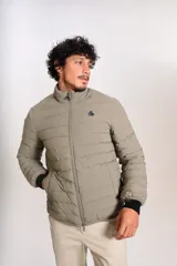 Campera puffer de corte clásico en color beige, con cierre frontal, cuello alto y puños elásticos. Presenta un diseño acolchado horizontal y un pequeño logo bordado en el pecho.