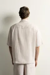 Camisa de lino color blanco, con ajuste relajado, cuello bowling, manga corta y cierre frontal con botones.