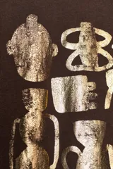 Camiseta de manga corta y cuello redondo, color marrón oscuro, con estampado frontal metalizado en tonos dorados que simula figuras de cerámica o arte tribal, y texto inferior que dice "Echoes in Gold".