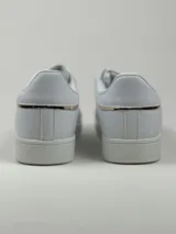 Zapatillas deportivas de cuero sintético en color blanco, beige y negro, con cordones y aplique decorativo dorado con forma de moño.