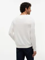 Sweater de punto liso en color blanco marfil, con cuello redondo, mangas largas y puños y dobladillo acanalados.