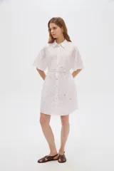 Vestido corto de algodón color blanco con diseño de broderie, cuello camisero, cierre frontal con botones, mangas cortas y lazo ajustable en la cintura.