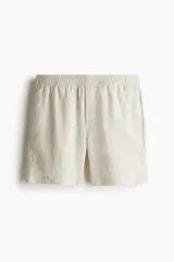 Short de lino liviano color beige, con cintura elástica y cordón oculto para ajustar. Presenta cierre decorativo, bolsillos laterales y un bolsillo trasero insertado. Corte estándar.