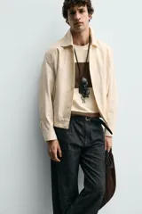 Cazadora boxy fit color beige, confeccionada en tejido de algodón y lino. Presenta cuello solapa, manga larga con puño abotonado, bolsillos de vivo en la cadera y bajo con elásticos laterales. Cierre frontal de botonadura.