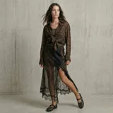 Falda midi de corte irregular con estampado de cuadros en tonos marrones. Presenta una superposición de encaje negro en el lateral y en el ruedo, aportando un diseño sofisticado y texturizado.