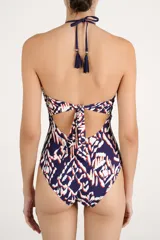 Malla enteriza de color azul marino con estampado geométrico abstracto en tonos blancos y anaranjados, escote en U pronunciado con detalles de bordado trenzado y tirantes halter con borlas colgantes.