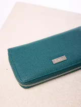 Billetera rectangular de cuero sintético con textura granulada, color bordó. Cuenta con cierre perimetral metálico y placa metálica con el logo de la marca en el frente.