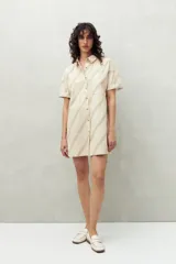 Vestido camisero corto color verde claro con estampado de hojas en blanco. Tiene cuello camisero, cierre frontal con botones y corte recto.