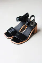 Sandalias negras de cuero charol, con tira ancha sobre los dedos y tobillo con hebilla metálica. Taco de madera.