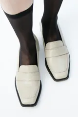 Mocasín de cuero color crema, con punta cuadrada, suela cuadrada negra y tacón bajo.