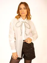 Camisa blanca de manga larga con cuello clásico y moño de strass en el frente.