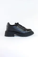 Zapatos de cuero negro con cordones, diseño robusto y suela track dentada. Presentan un detalle metálico en el centro de los cordones.