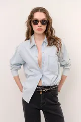Camisa de jean de corte oversize, color celeste claro, con cierre frontal de broches metálicos y un bolsillo aplicado en el pecho.