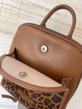 Mochila de cuero marrón con estampado animal print dorado y detalles en cuero liso. Cuenta con cierre superior, asa de mano y correas ajustables para los hombros.