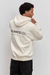 Buzo con capucha de corte holgado, color crema, con bolsillo frontal tipo canguro y pequeña estampa tipográfica en el pecho.
