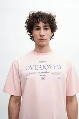 Remera manga corta color rosado con cuello redondo y estampado con la palabra "Overjoyed" en azul.