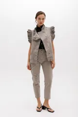 Chaleco de denim azul con estampado paisley, sin mangas, con volados en hombros y cuello, cierre frontal con botones metálicos y bolsillos laterales.