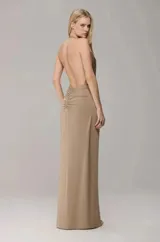 Vestido largo de fiesta color beige, con diseño de frente única, escote profundo en V y detalle de nudo en la cintura. Presenta una falda fluida con tajo frontal central.