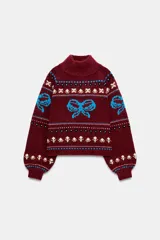 Jersey de punto con cuello subido y manga larga con puños ajustados. Presenta un diseño jacquard con motivos de lazos en color azul y detalles florales en tonos crema sobre una base de color bordó.