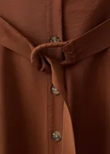 Vestido midi de color marrón, con diseño evasé, cuello camisero y cierre frontal con botones. Presenta un cinturón ajustable a la cintura y un diseño sin mangas con tirantes anchos.