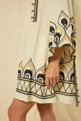 Minivestido blanco de lino con escote en V, mangas anchas acampanadas y bordados dorados en los puños, el dobladillo y el cinturón ajustable.