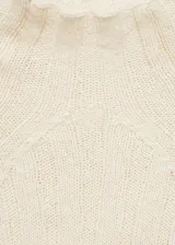 Buzo de punto acanalado color crema con diseño desagujado, cuello perkins y mangas largas acampanadas.