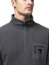 Buzo de polar gris oscuro con cuello alto y medio cierre frontal. Presenta un bolsillo en el pecho con cierre y detalles en nylon, además de bolsillos laterales con cierre.