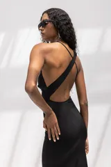 Vestido largo negro de corte al cuerpo, con escote halter y cuello drapeado. Presenta una silueta entallada que se ensancha suavemente hacia el ruedo.