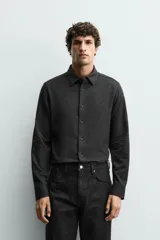 Camisa de corte relajado confeccionada en tejido de algodón con textura. Presenta cuello italiano, manga larga con puños abotonados y cierre frontal mediante botonadura.