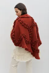 Chal de lana color terracota, con diseño amplio y envolvente. Presenta volados decorativos que recorren toda la prenda, aportando textura y movimiento.